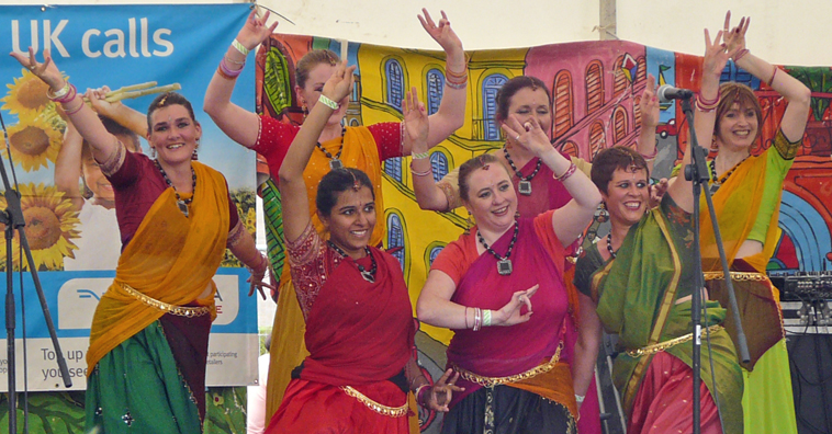 Seven women dancers, dressed in different primary colours, strike a pose at the end of their performance