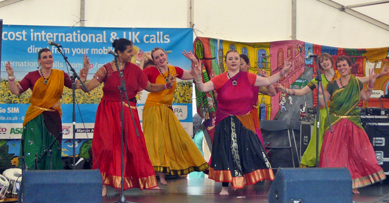 Seven women dancing in different primary coloured costumes