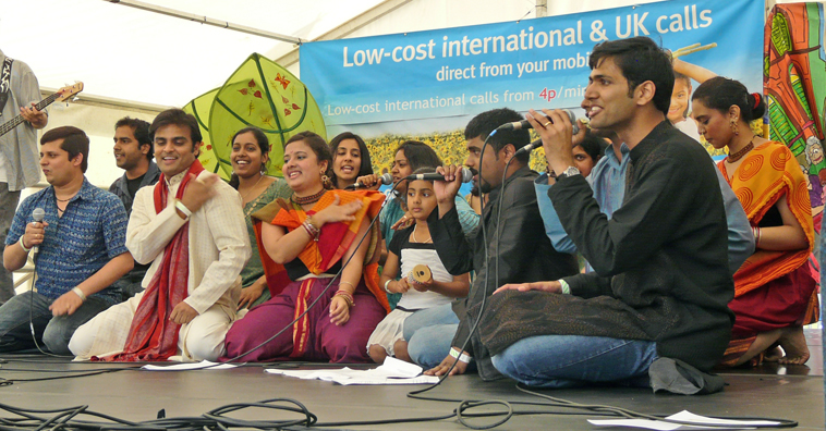 Two rows of men, women and children, kneeling and performing a song with hand gestures