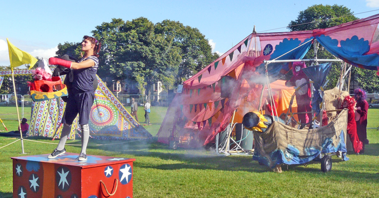 Woman standing on a red trunk as  four lions creep up behind her with  a ship that has a smoking cannon