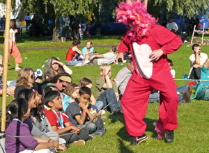 Cross legged children watch a red and pink lion staling