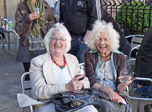 Two women laughing  and holding their glasses as the wind blows their hair