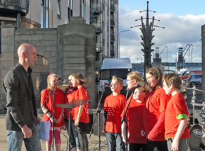 Eight children in red t-shirts with a wrought iron sculpture and Leith Docks in the distance