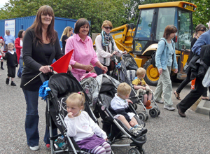 Three women pushing buggies with small children in, in formation