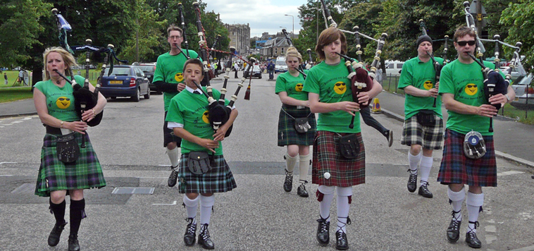 Pipers in kilts with  the distinctive green Sunshine on Leith tee shirts with the  smiley sun with dark glasses logo
