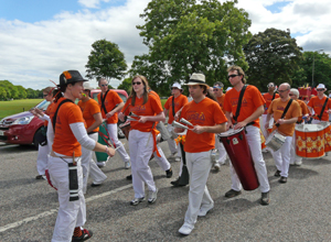 Drummers marching in oragnge tee shirts and white trousers