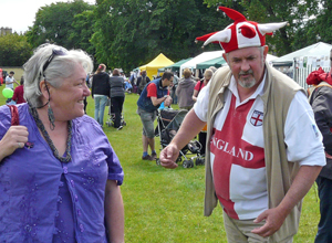 Man in England St George's cross tee shire, with red and white jester's hat, posing as his laughing wife watches on