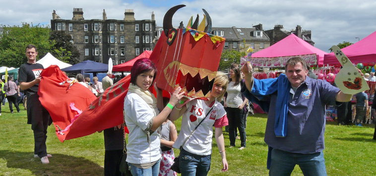 Two young women hold up the head of the red Citadel dragon as  Willie Barr watches on waving a giant hand