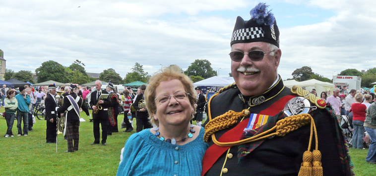 Man in full braided uniform, smiling with woman in blue dress to his right hand side