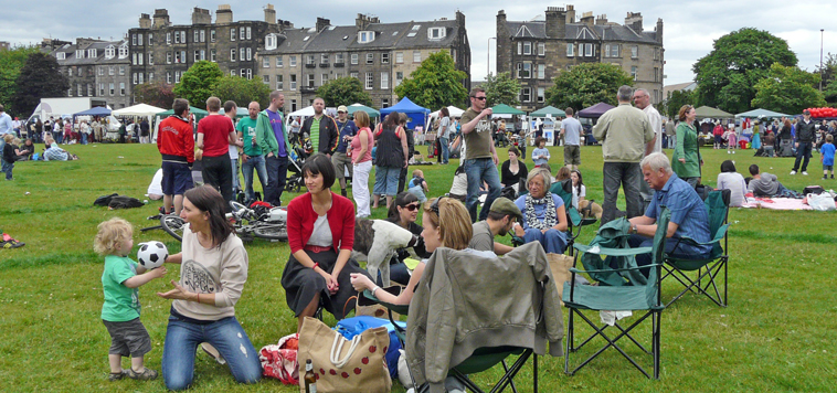 People sitting in camp chairs with young children picnicking with Links Gardens visible in the distance