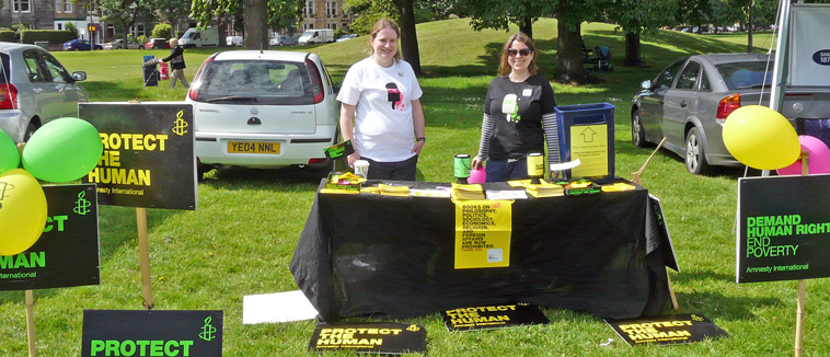 Stall with two women and various "Protect the Human materials on black with line and yellow print