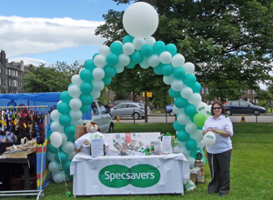 Woman standing by a tombola stall with an arch of green and white balloons
