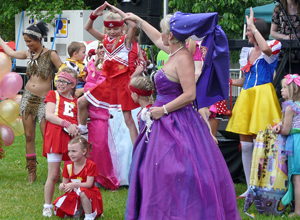 Girl majorettes in red costumes forming a  human pyramid helped by a woman in purple ball gown and wimple
