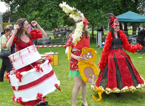 Three costumed women dancing, one of them as a giant cake