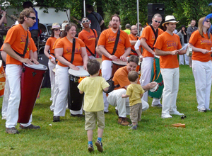 Drummers in orange tee shirts and white trousers joined by two little boys