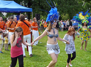 Tow girls dancing with woman in white and blue costume with blue feathered head dress
