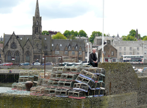 Man dressed in black sitting  atop  lobster pots by the  harbour entrance