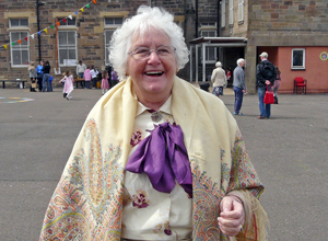 Smiling ady in cream with a cream coloured Paisley shawl and a purple scarf