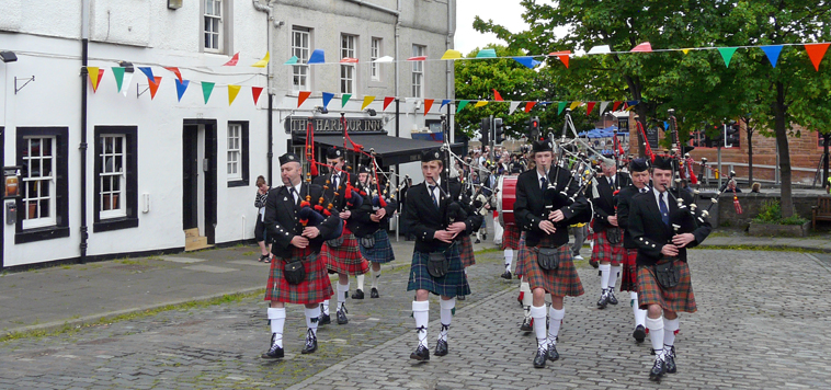 Pipers marching up the cobbled slope with  The Harbour Inn in the background