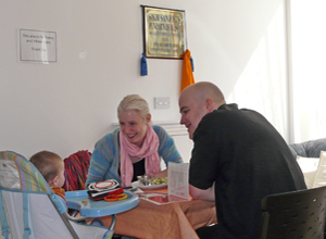 A young woman and man seated at a table smiling at an infant in a high chair