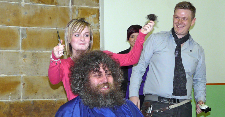 Finlay Smith holding up the first lock of Dave's hair as Simon Hill and Vicki watch on