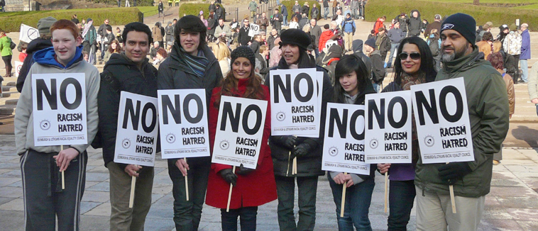 Eight young women and men holding pladcards saying "NO TO RACISM HATRED" in front of the Ross Bandstand