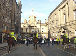 Three mounted police officers with marchers and the Bank of Scotland HQ behind them