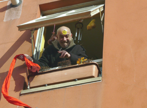 Man with an Anti Nazi League sticker on his shaved head leaning out of an upper window, waving a red scarf