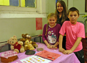 A boy and a girl from Victoria and a girl from Trinity  with a pink decorated cake and teddy bears