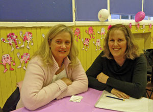 Two seated women smiling with pink figures on the wall behind them