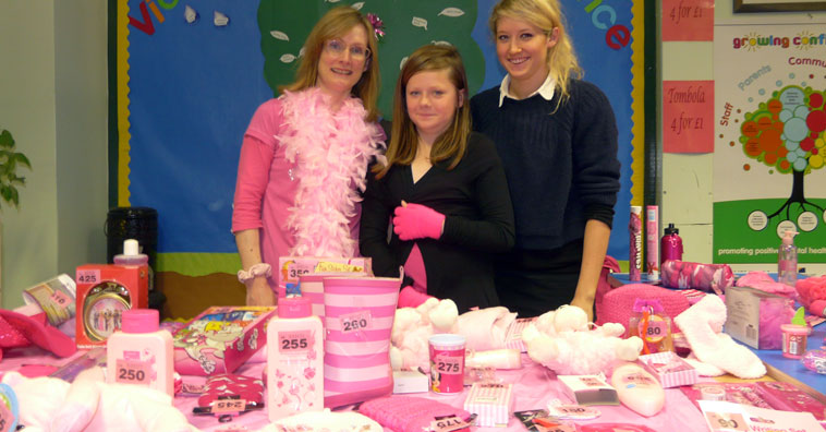 Women in pink feather boa and two girls smiling behind a table covered in pink bathroom products, toys and many other items.