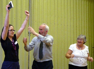 Woman with arms raised, as man reaches to pull her arms down, with smiling woman watching on