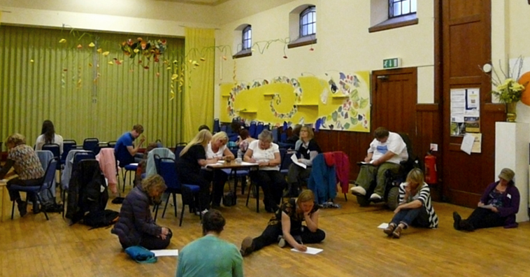 Around 20 people seated on chairs and on the floor, writing and reflecting