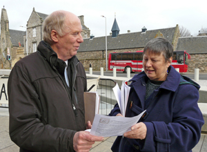 Malcolm in winter wear talking with Sally in an indigo cast with Holyrood in the background