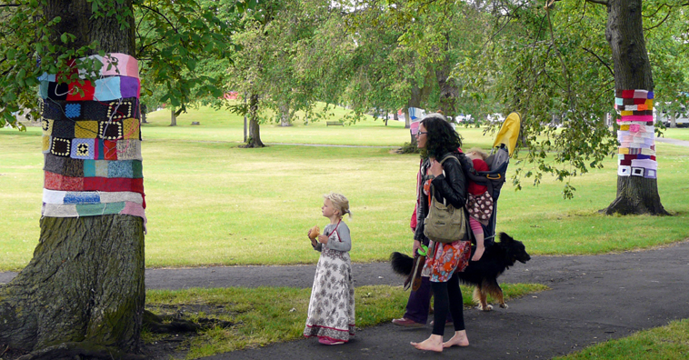 A small girl, a woman and a dog look at a newly installed tree blanket on Leith Links
