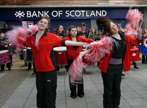 Three cheerleaders in red and black with arms extended twirling pink pom poms