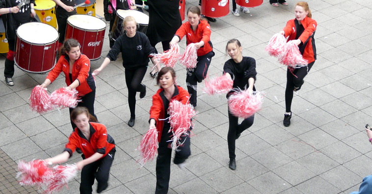 Two rows of cheerleaders in black trousers and red tops with pink pom poms