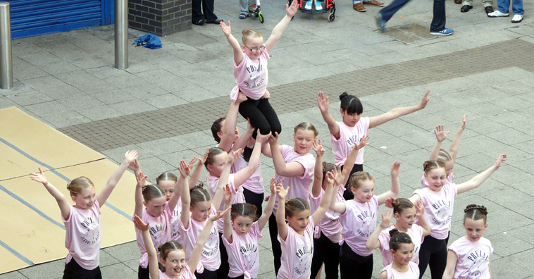 Primary school age girls in pink shirts lift a trouper aloft
