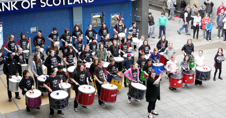 The front rows of the Pulse of the Place samba drummers in front of the Bank of Scotland in the Kirkgate