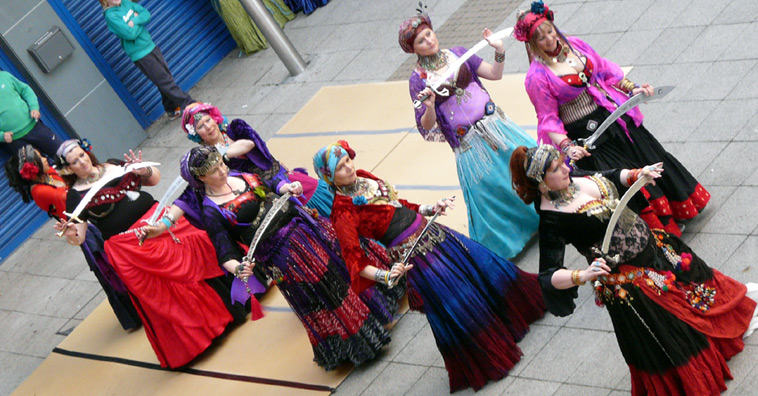 Women dancing American Tribal style in pink, black, blue, red and purple costumes with turbans - and swords
