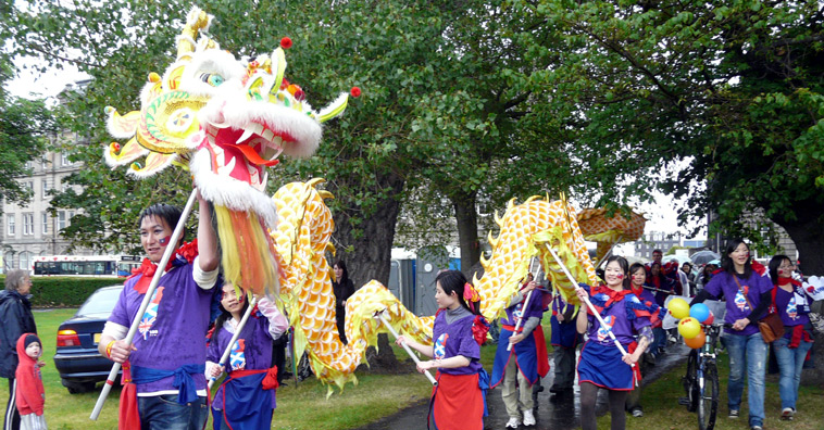 Edinburgh Taiwanese Students in purple tee shirst carrying a white and golden dragon through the trees onto Leith Links