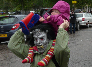 Man in a demon monster mask giving a high shoulder to a pink clad toddler