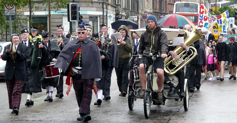 Band members in waterproof capes marching land playiing instruments