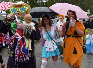 Two women dressed as Wilma and Fred Flintsone with a man decked in Union Jacks carrying a baby doll
