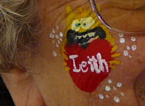 Yellow monster grinning and holding a red heart with the word Leith painted on it