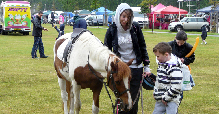 A young woman in white hoodie and black leather jacket holds Hamish, a white and brown horse as a boy in a black and white striped rugby shirt looks at Hamish