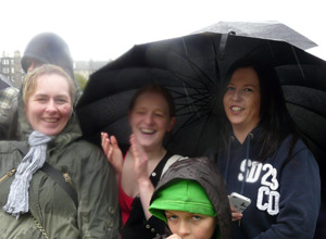Three smiling women gathered round an umbrella