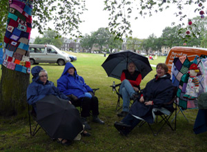 Four people sitting under rugs and umbrellas