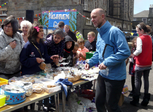 Pepple standing the length of a cake stall being served by a man in blue
