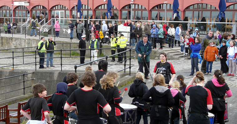 View of Pulse of the Place, dressed in black and red, from behind looking across to the crowds along the harbour wall